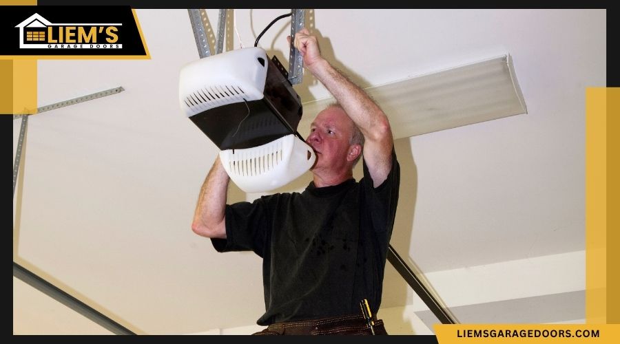 A technician in a black shirt inspecting a white garage door opener motor mounted on a ceiling