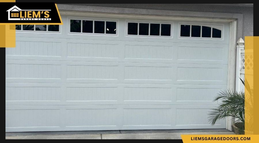garagedoorclearance White carriage style sectional garage door with a top row of grid windows branded with the Liem's Garage Doors logo.